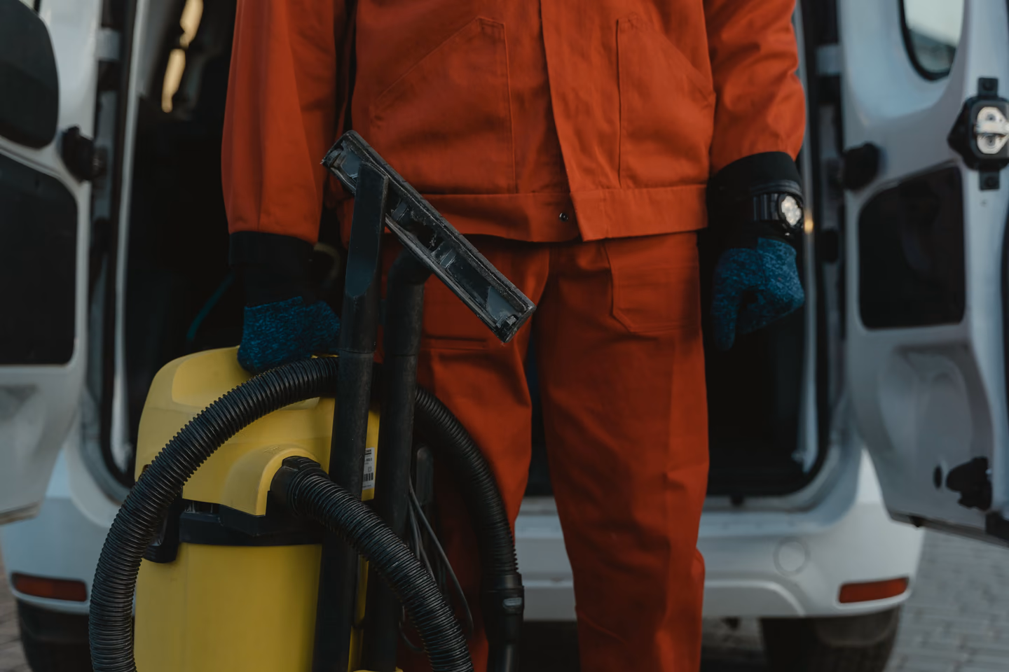 Mitarbeiter im orangefarbenen Arbeitsanzug mit Nasssauger vor einem geöffneten Transporter