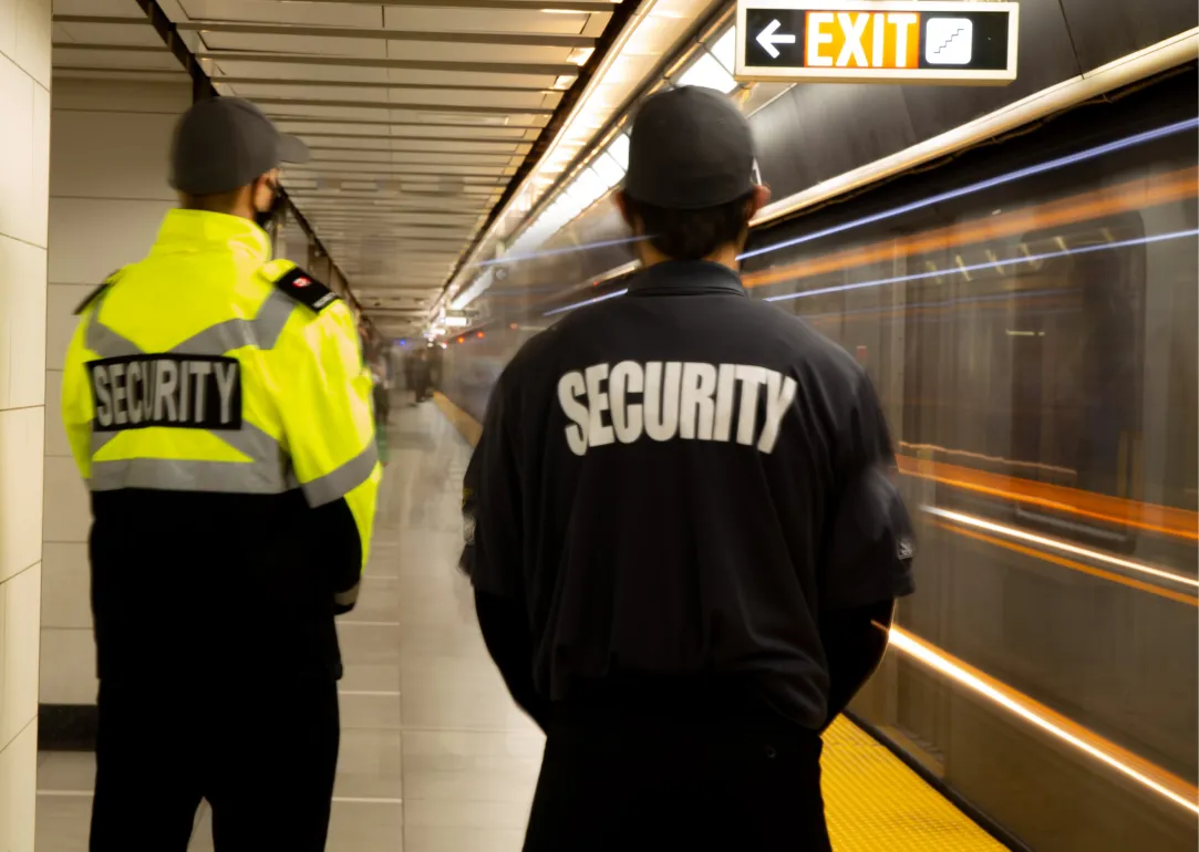 Zwei Securityarbeiter in einem Bahnhof von hinten fotografiert
